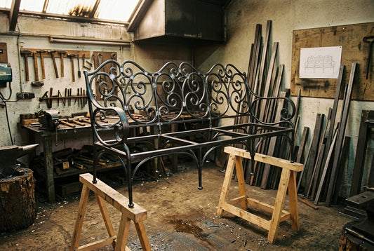 Structure nue d’un canapé trois places en fer forgé sur tréteaux dans l’atelier, avant patine