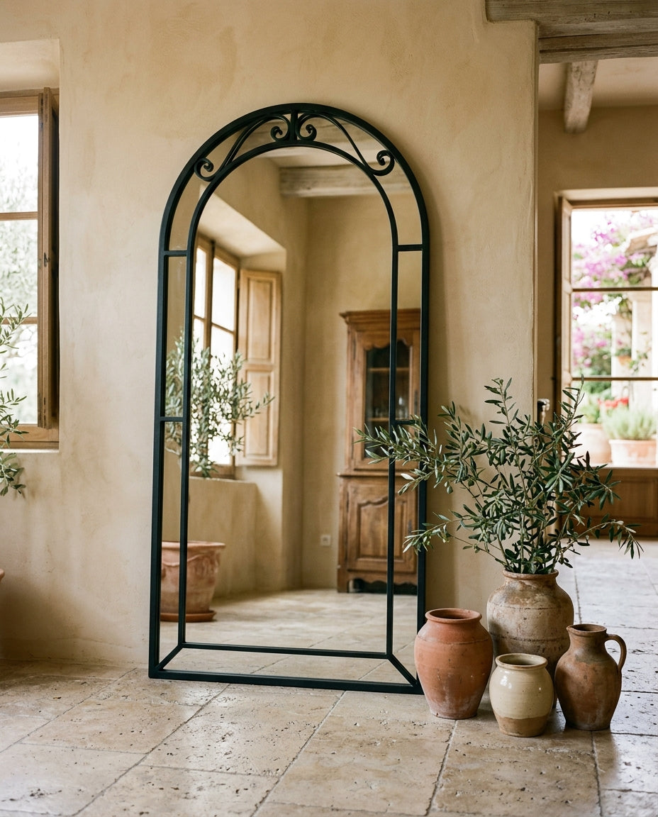 Grand miroir arche au cadre fer forgé noir posé contre un mur, intérieur méditerranéen
