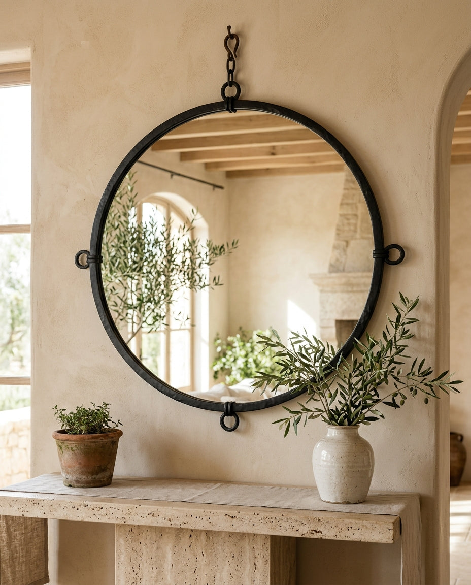 Miroir rond au cadre fer forgé noir au-dessus d'une console travertin, intérieur méditerranéen