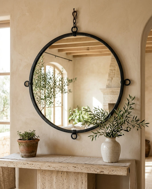Miroir rond au cadre fer forgé noir au-dessus d'une console travertin, intérieur méditerranéen